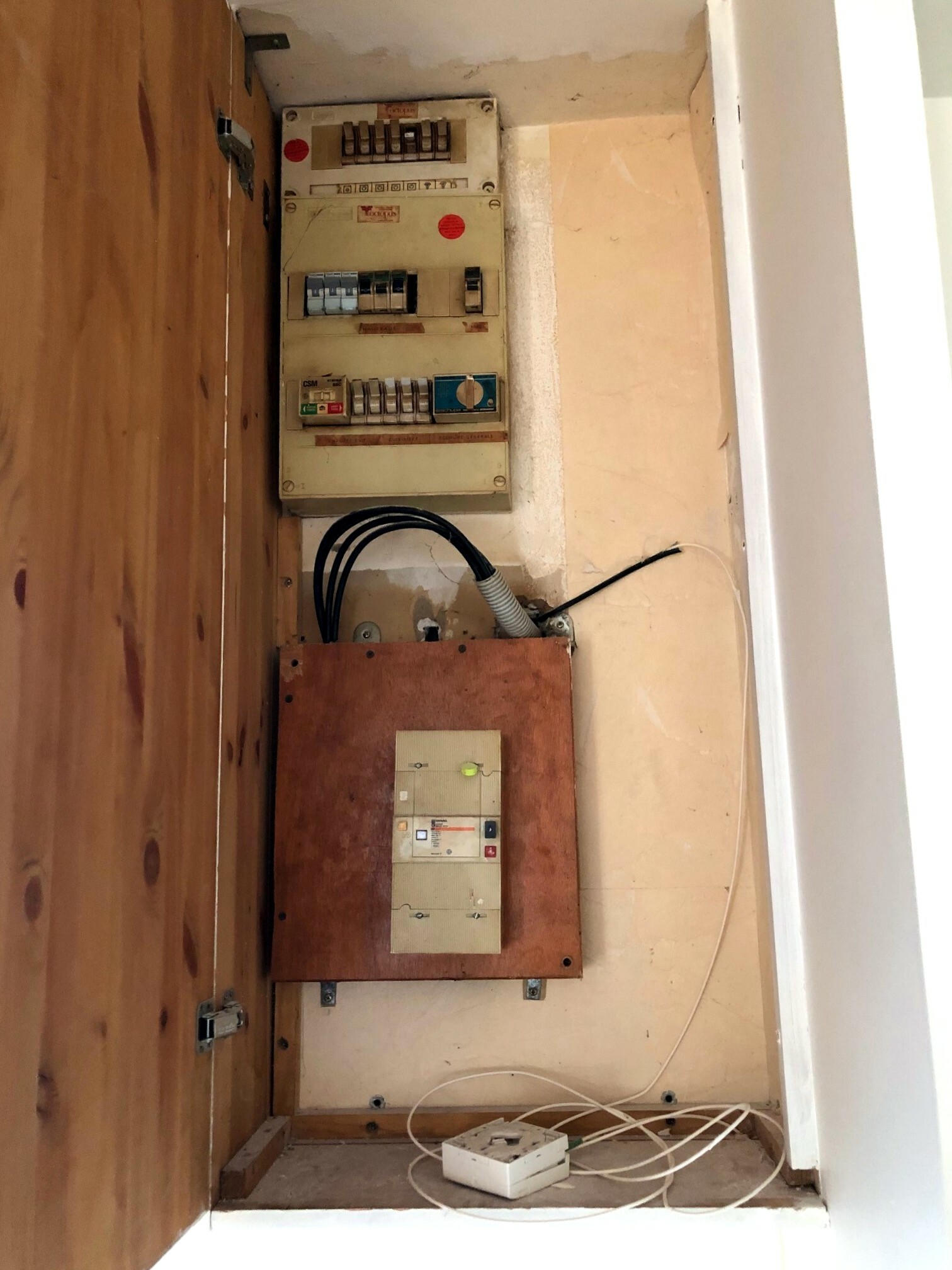 Tableau électrique ancien dans un renfoncement, câbles visibles au premier plan